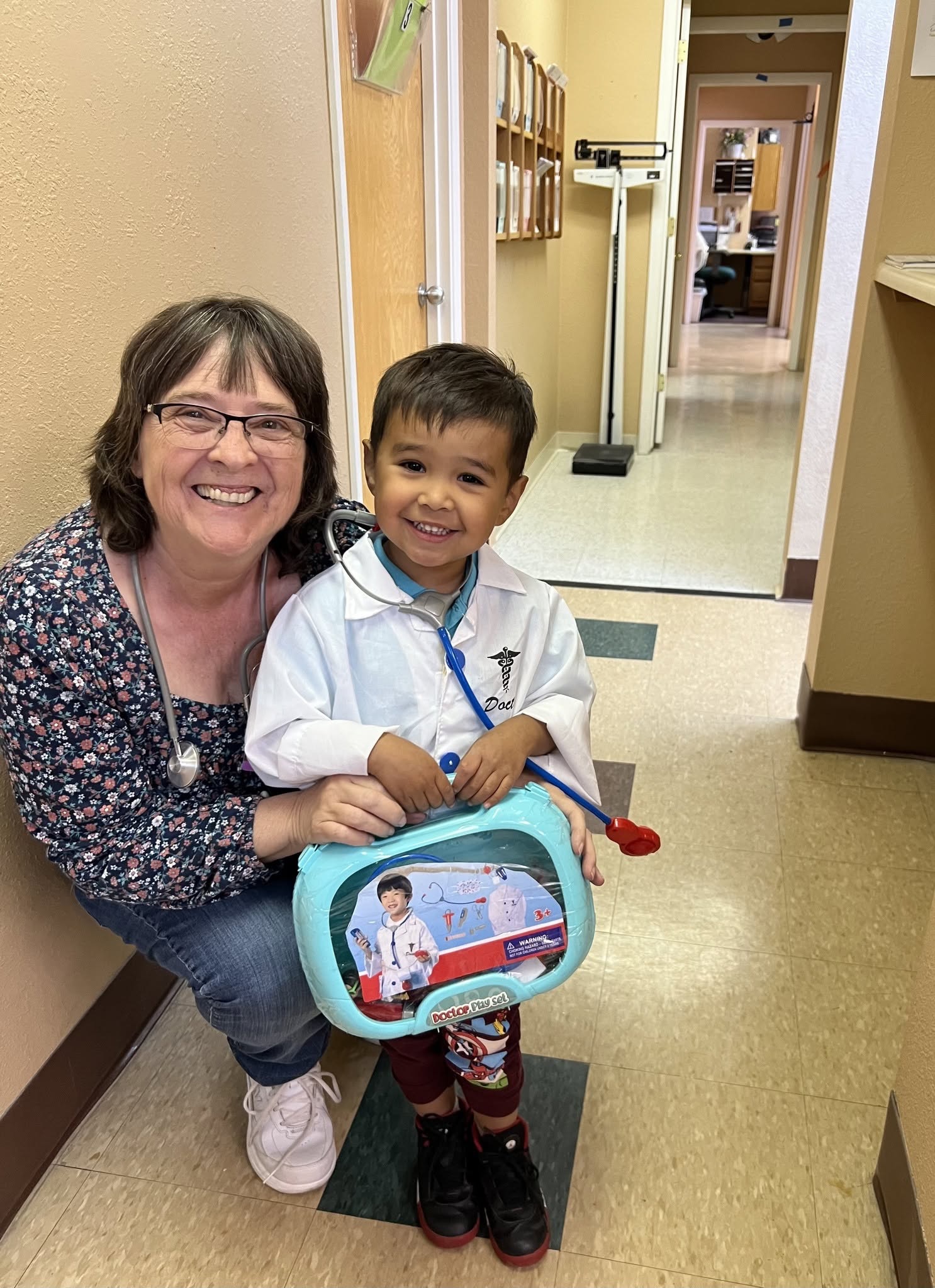 A clinic team member smiling with a young visitor dressed as a doctor